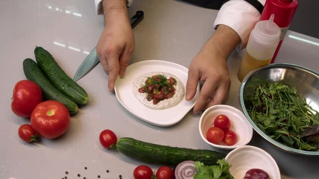 Chef of upscale gourmet restaurant presents masterpiece of culinary excellence and classic dish: steak tartare, served with white sauce based on sour cream, garnished with herbs and garlic