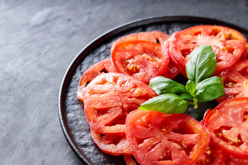 Juicy Tomato Slices with Fresh Basil Leaves on Black Plate, Dark Grey Textured Background, Top View, Copy Space