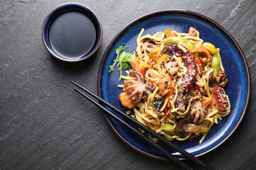 Stir-fry noodles with sea food, vegetables and soy sauce on dark textured table, top view