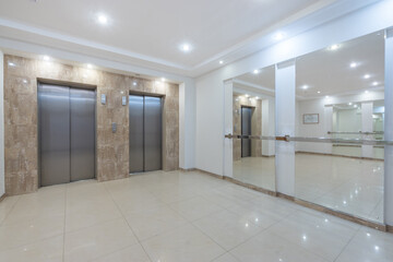 Office hall with mirrors on the wall and two modern elevators. Bright room decor.