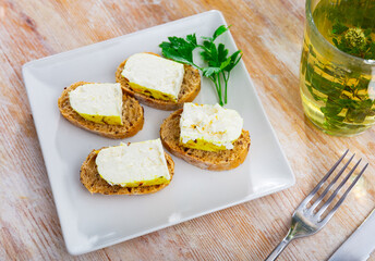 There are sandwiches with Lithuanian cheese and sesame seeds on square plate. Homemade snack for picnic, buffet. Snack is complemented with herbal mint tea.