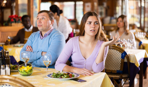 Man and his wife sitting at dining table in restaurant and quarreling.