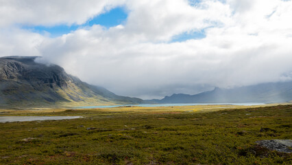 Beautiful breathtaking view to the mountain valley with fresh rain and sunshine through tearing clouds over scenic nordic wilderness with lakes and meadows in swedish Lapland nature in autumn. Sweden