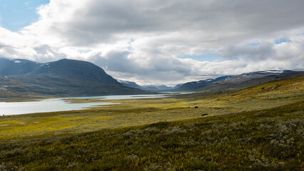 Breathtaking scenic view to the wide mountain valley with lake and mountains on horizon, grassy meadows and dramatic sky seen while hiking Kungsleden trail in nordic nature of swedish Lapland. Sweden