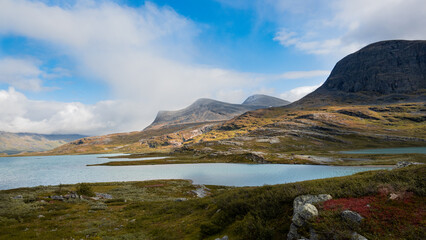 Beautiful nordic swedish landscape during autumn season with blue sky, mountains, sunshine over grassy meadow and azure lake evokes far north, wilderness, remote and adventure when hiking Kungsleden.
