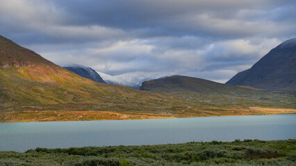 Clouds over glacier and mountains with calm lake beautifuly englighted by autumn golden light during evening in swedish nordic wilderness of Lapland evokes adventure, solitude and harsh landscape.