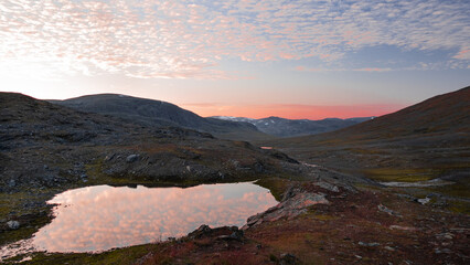 Beautiful colorful sunset over the silent calm mountain valley of Tjäktja with small lake, red clouds and grass highland nordic nature, found on the trail of Kungsleden in Sweden.