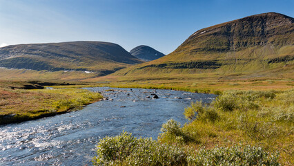 Breathtaking scenery of nordic fragile arctic nature with river and mountains raising from tundra during beautiful autumn day in northern Sweden seen on hike of Kungsleden trail in Lapland landscape