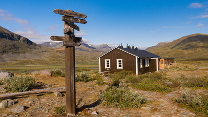 Wooden signpost and typical wooden nordic house provides shelter in remote wilderness for hikers in...