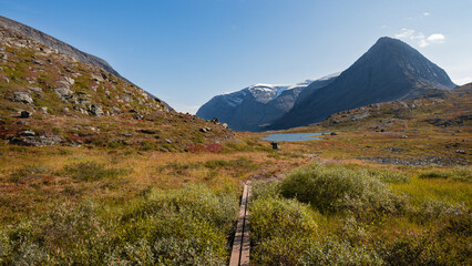Breathtaking view to scenic epic swedish nature with plank path, tall peaks with snow, colorful autumn landscape and small lake evokes adventure, exploration, remoteness, wilderness in swedish Lapland