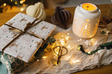 Merry Christmas and Happy holidays! Stylish christmas gift, glowing lantern, modern paper ornaments on table with golden christmas lights. Atmospheric christmas eve, holiday magical time
