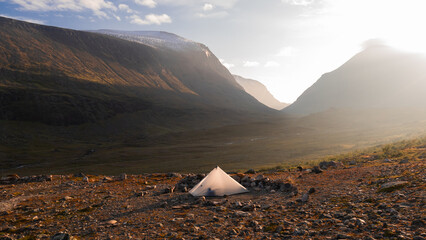 Tarp tent placed in nordic swedish scenic landscape on Kungsleden trail with deep valley and steep...