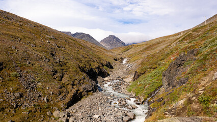 Obraz premium Creek running through rocky valley with scenic view towards the mountains and peaks on horizon during beautiful autumn day in swedish lapland nature near Kebnekaise on the way to Tarfala 