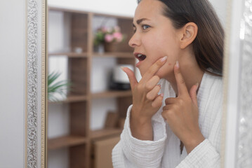 A distressed woman gazes into the bathroom mirror, feeling unhappy about her skin concerns. 