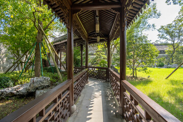 A traditional Chinese covered walkway with ornate wooden latticework railings overlooks a peaceful...
