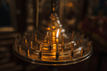 Burning candle in gilded candelabrum in Christian church, temple. Photography, religion concept.