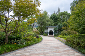 A stone pathway or a paved footpath in a public park winds through a lush, landscaped garden, and leads to a small gazebo or shelter. Background texture of hardscape or landscaping design.