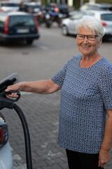 Smiling Senior Woman Charging Electric Vehicle in Parking Lot