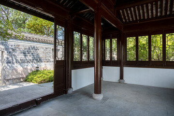 Ornate latticework windows, wooden pillars, and a tiled roof adorn the interior of a traditional Chinese garden pavilion. An open door with a view of the Asian courtyard wall. Copy space for design
