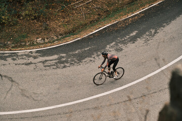 Cyclist on a scenic road curve, enjoying a solo ride through autumnal landscape.  High-angle shot emphasizing the winding path and cyclist's journey.