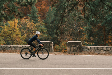 Fototapeta premium Woman cyclist rides road bike through scenic autumn landscape. Perfect for travel, sports, and healthy lifestyle themes. Romania. Carpathian Mountains. Transylvania