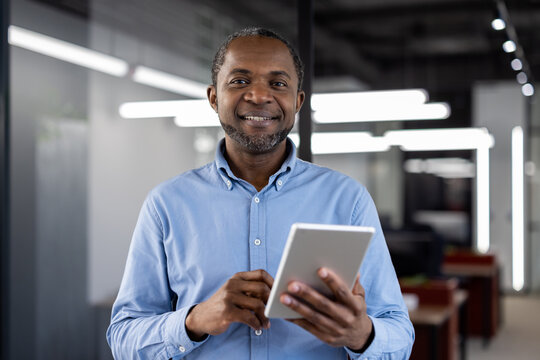 Mature african american businessman using digital tablet in modern office. Confident expression, business professionalism, and technology highlight his expertise. Ideal for business or tech themes.