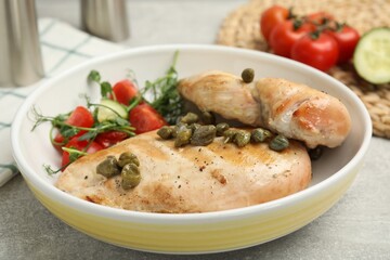 Delicious cooked chicken fillets with capers and salad on light grey table, closeup