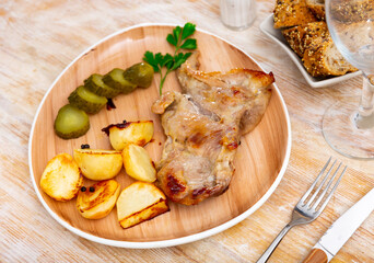 Appetizing piece of fried pork with marinated cucumber and potatoes served on plate