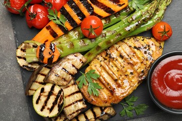Delicious grilled vegetables and chicken breast served with sauce on grey table, top view