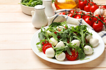 Tasty salad with arugula, spinach, mozzarella cheese and tomatoes on wooden table, closeup