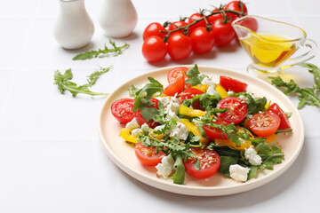 Tasty salad with arugula, cheese and vegetables on white tiled table