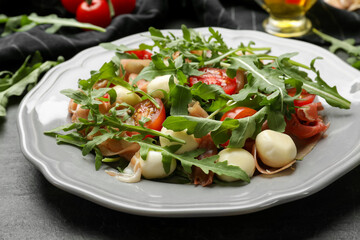 Tasty salad with arugula on dark textured table, closeup