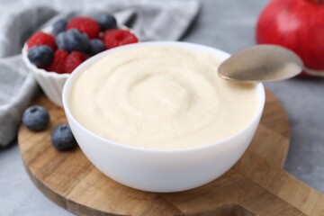 Tasty cooked semolina porridge in bowl and berries on grey table, closeup