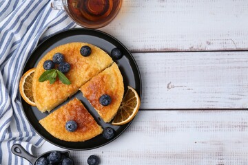 Delicious semolina cake with blueberries and orange slices on white wooden table, flat lay. Space for text