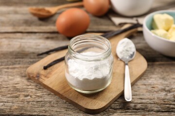 Baking powder in jar and spoon on wooden table, closeup