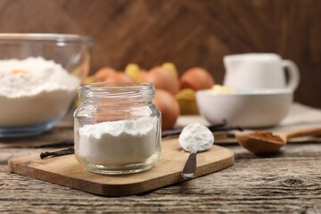 Baking powder in jar and spoon on wooden table, closeup