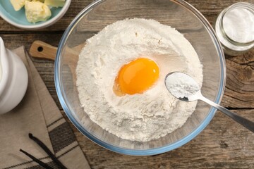 Adding baking powder into bowl at wooden table with other products, top view
