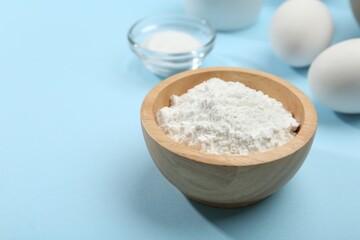 Baking powder in bowl, eggs and salt on light blue background, closeup. Space for text