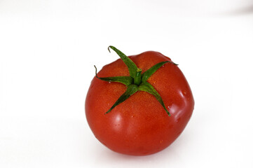 A vibrant red tomato with a fresh green stem placed on a clean white surface amidst kitchen preparations