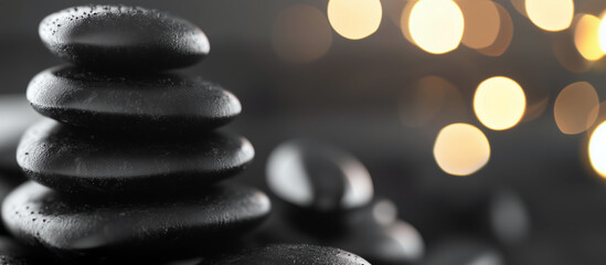 Obraz premium Black spa stones are stacked elegantly against a softly lit background. Smooth black spa stones arranged artistically with gentle bokeh lights.