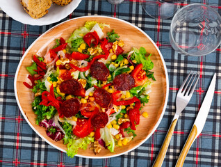 There are large pieces of fresh vegetables and sliced chorizo sausage on plate. Vitamin salad of fresh vegetables, china cabbage, corn, chorizo and Bulgarian pepper