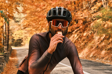 Cyclist takes a break to eat a snack during an autumn ride.  Golden leaves frame the athlete in...