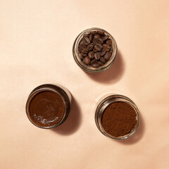 Roasted, ground and brewed coffee in jars on a beige background