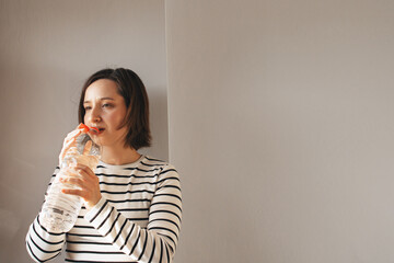 Fototapeta premium Woman Drinking Water From A PET Plastic Bottle, Demonstrating The New Tethered Caps On Plastic Water Bottles, Refreshing Herself At Home. New Eu Regulation
