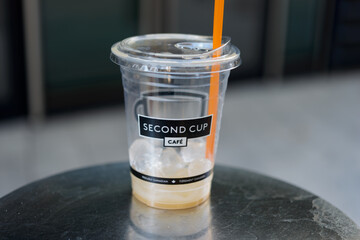 Fototapeta premium ice melts inside a discarded Second Cup Café plastic cold drink cup with lid and orange straw outside in Toronto, Canada