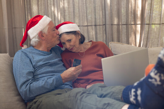 Christmas time, Elderly couple in Santa hats shopping online with laptop and credit card, at home
