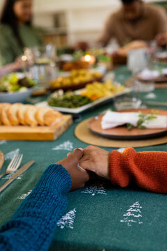 Christmas time, multiracial family holding hands at festive dinner table, at home