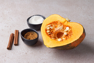 Cut raw orange pumpkin with seeds, cinnamon and sugar on a beige textured stone background. Preparing pumpkin for baking