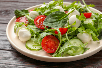 Tasty salad with arugula, spinach, mozzarella cheese and vegetables on wooden table, closeup