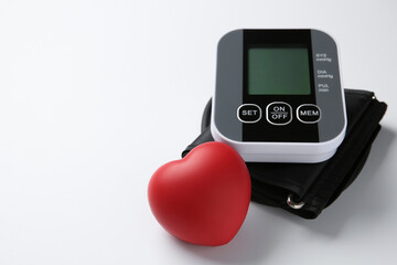 Blood pressure measuring device and squeeze heart on white background, closeup. Space for text